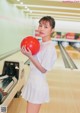 A woman holding a red bowling ball in a bowling alley.