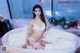 A woman in a white lingerie sitting in a bathtub.