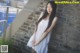 A woman in a white dress leaning against a brick wall.