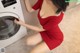 A woman in a red dress is putting something in a washing machine.