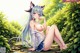 Anime girl with long blue hair sitting on a rock in the woods.