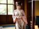 A woman in a pink kimono standing in front of a window.